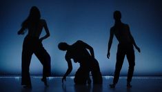 Colour image of silhouettes of three female dancers at different levels on blue-lit stage